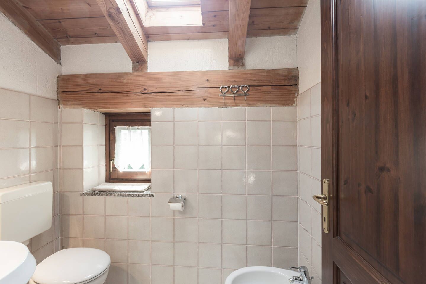 A bathroom with a wooden ceiling, a small window, and a wooden door.