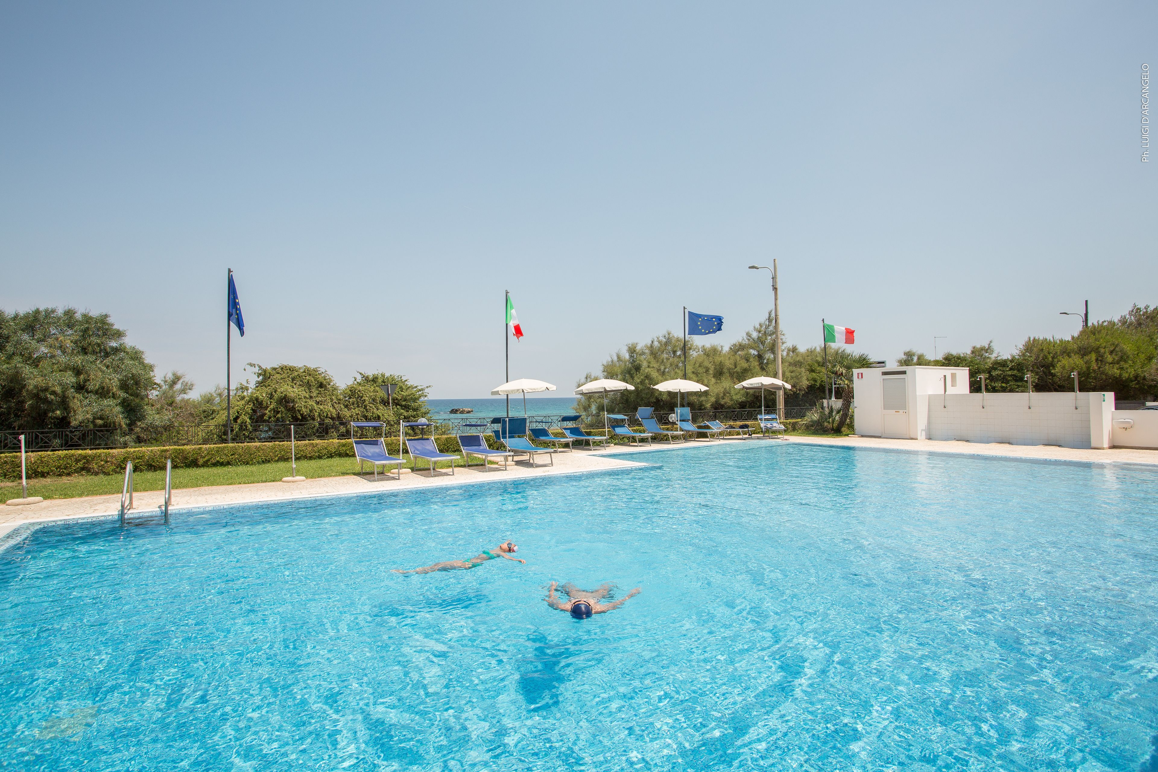 Ein Swimmingpool mit klarem, blauem Wasser, Liegestühlen und Flaggen.