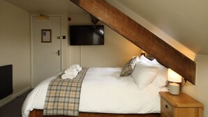 A bedroom with a bed, a television mounted on the wall, a wooden nightstand, and a door with a bulletin board. - The Avenue (Durham)