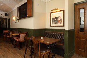 A dining area with wooden tables and chairs, a cushioned bench, and a framed artwork on the wall.