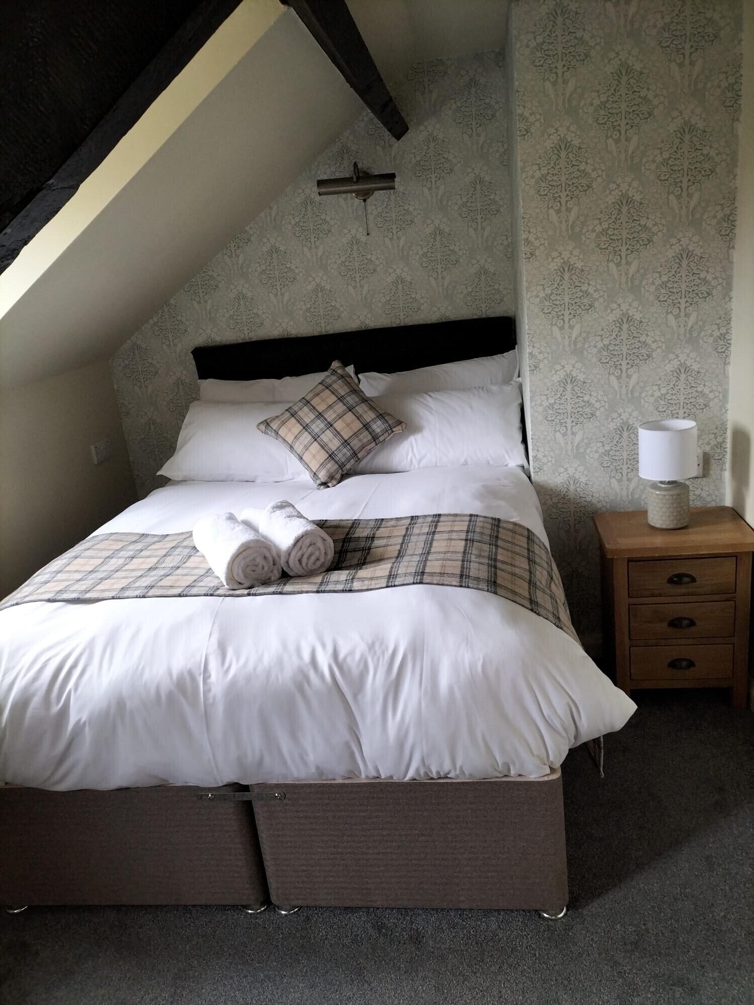 A neatly made bed with a plaid bedspread and pillows, a bedside lamp, and a nightstand with drawers.