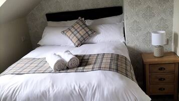 A neatly made bed with a plaid bedspread and pillows, a bedside lamp, and a nightstand with drawers.
