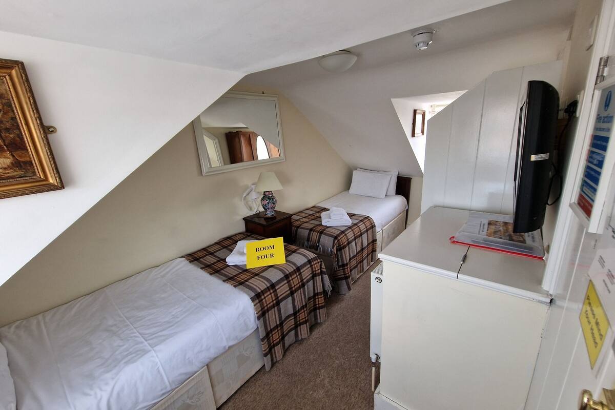 A compact room with two beds, a small table, a mirror, a TV, and a sign indicating 'ROOM FOUR'.