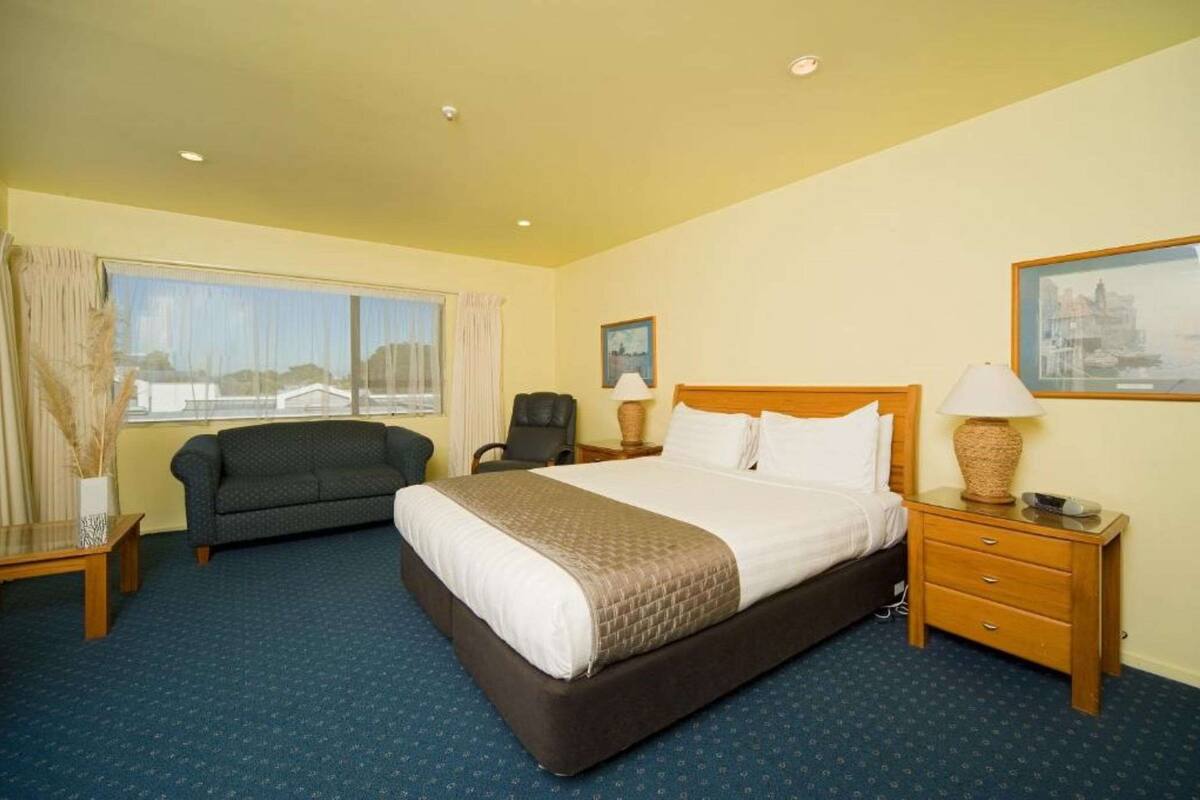 A hotel room with a large bed, a sofa, a chair, a desk, and a window with curtains.