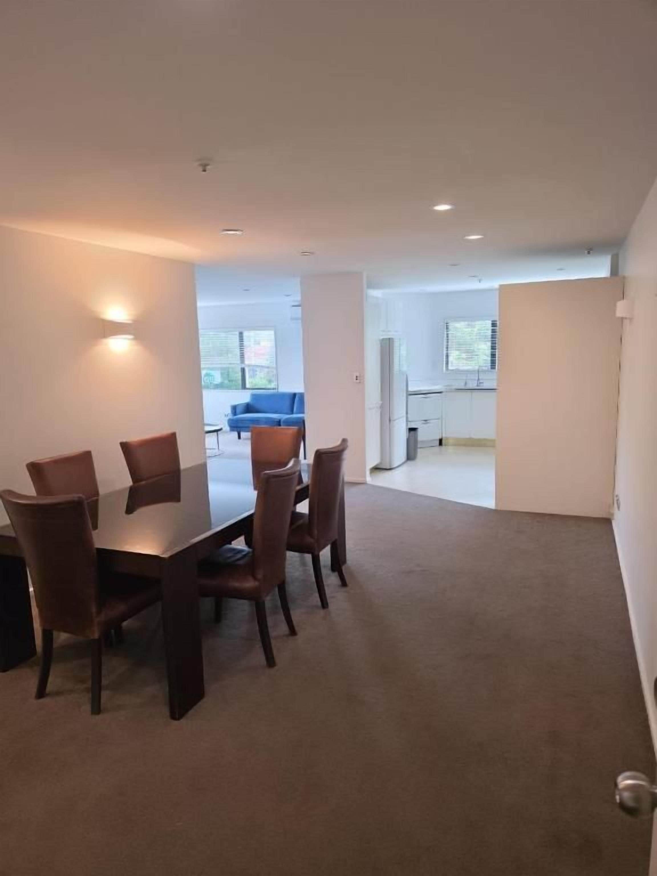 Un comedor con mesa y sillas, suelo alfombrado y vista a otra habitación.
