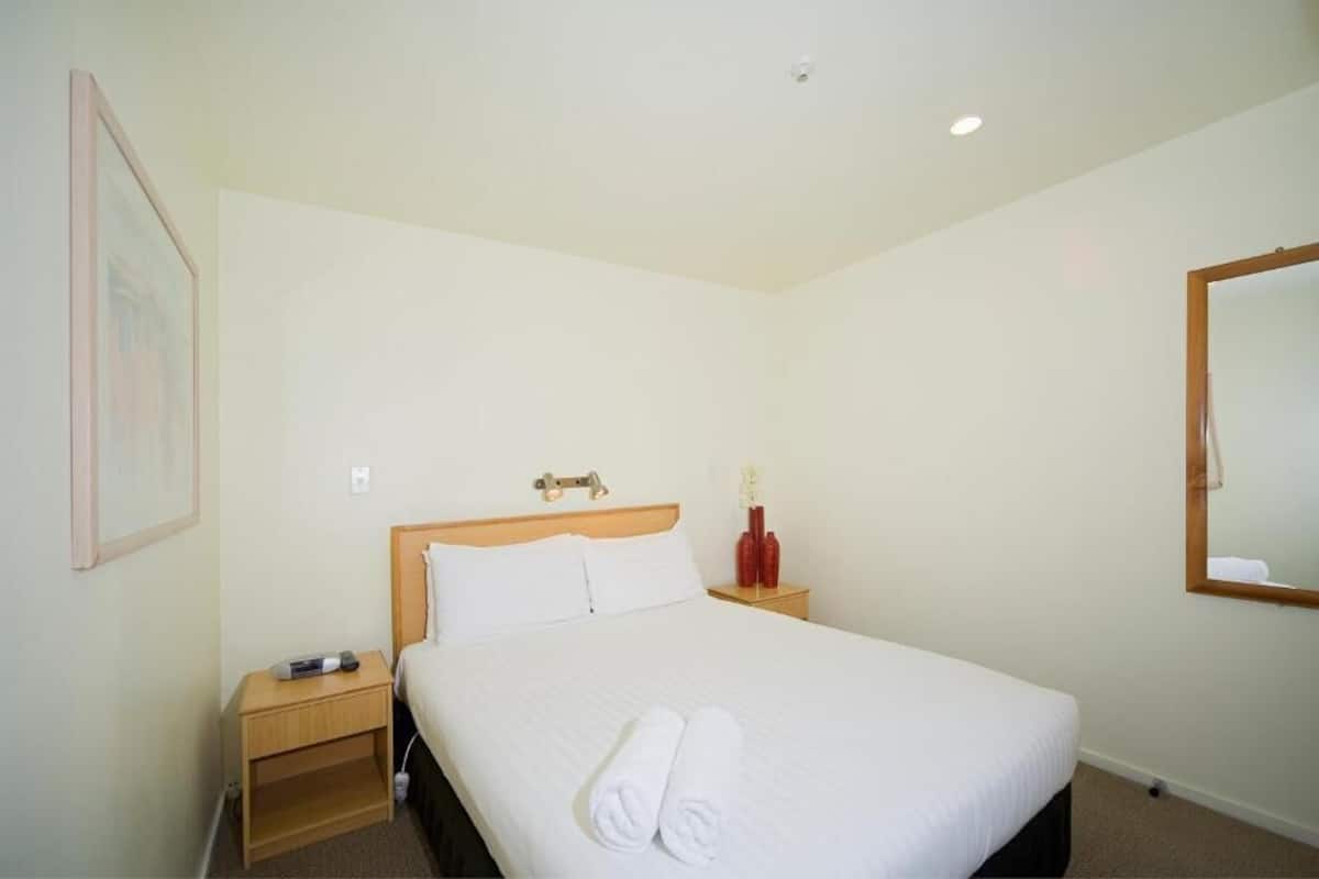 A hotel room with a single bed, a nightstand, a bedside table, a mirror, and a framed picture on the wall.