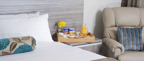 A hotel room with a bed, a bedside table with a tray of breakfast items, a chair, and a headboard.