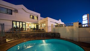 A modern hotel with a swimming pool, outdoor seating, and a large illuminated sign.