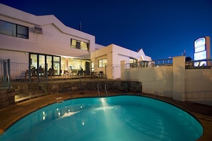 A modern hotel with a swimming pool, outdoor seating, and a large illuminated sign.