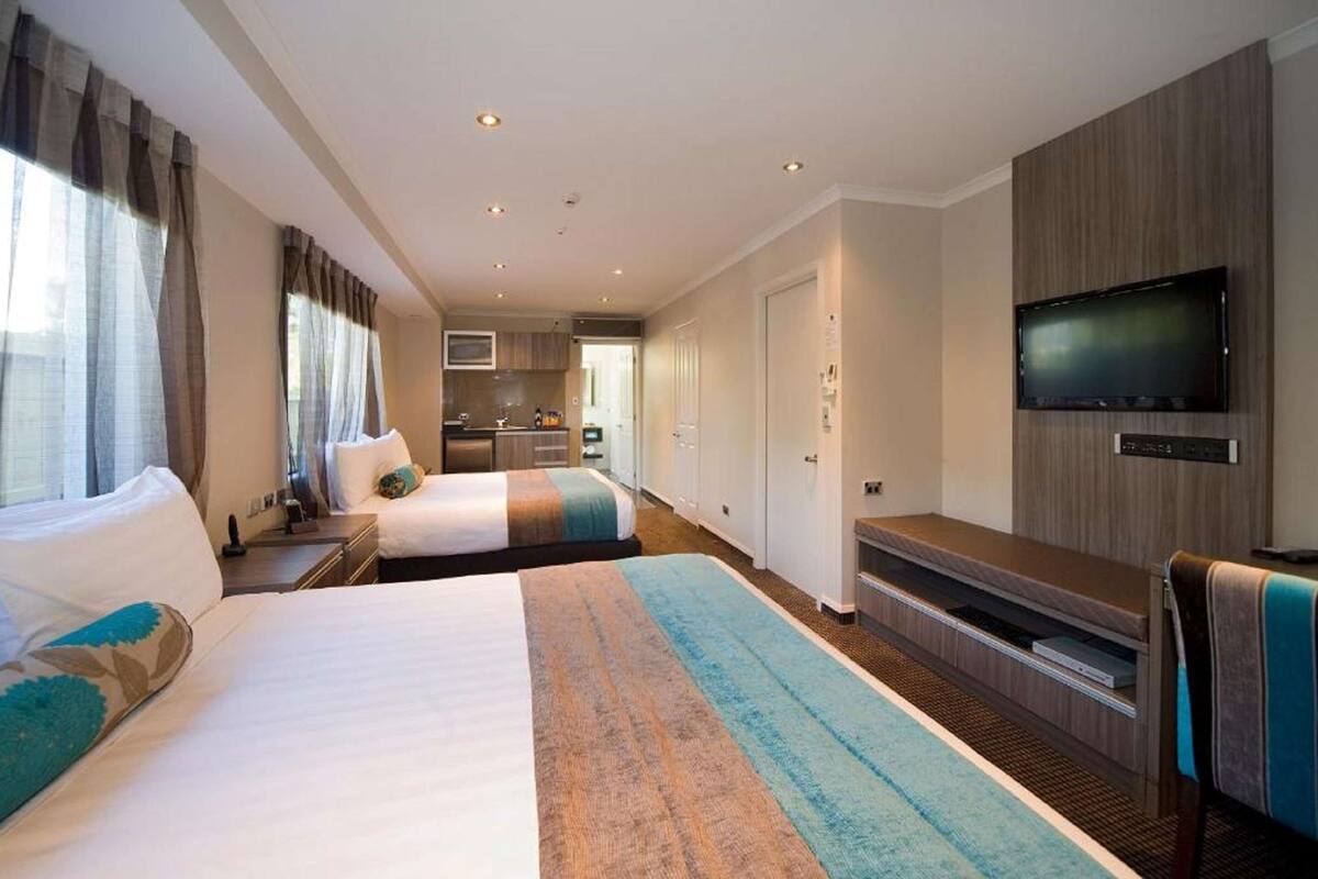 A hotel room with two beds, a TV, a kitchenette, and a bathroom.