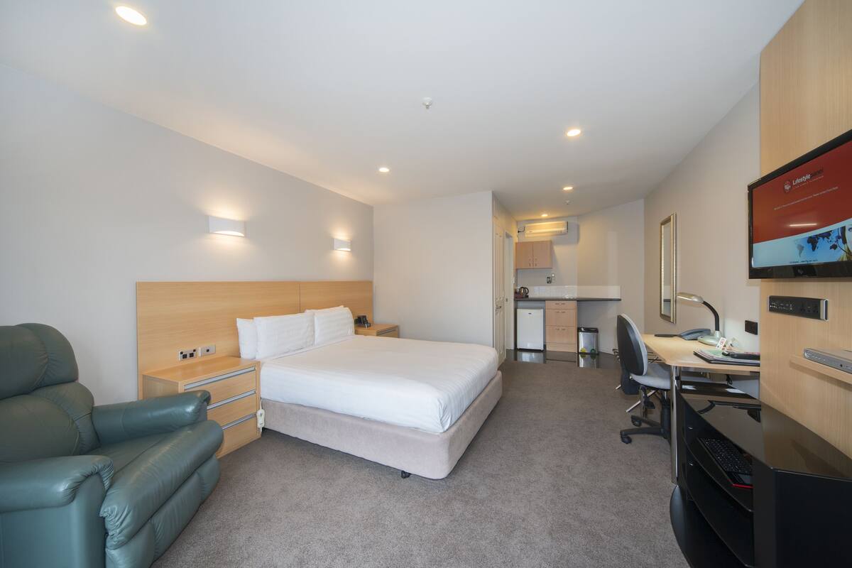 A hotel room with a bed, a desk, a chair, a sofa, and a TV on the wall.