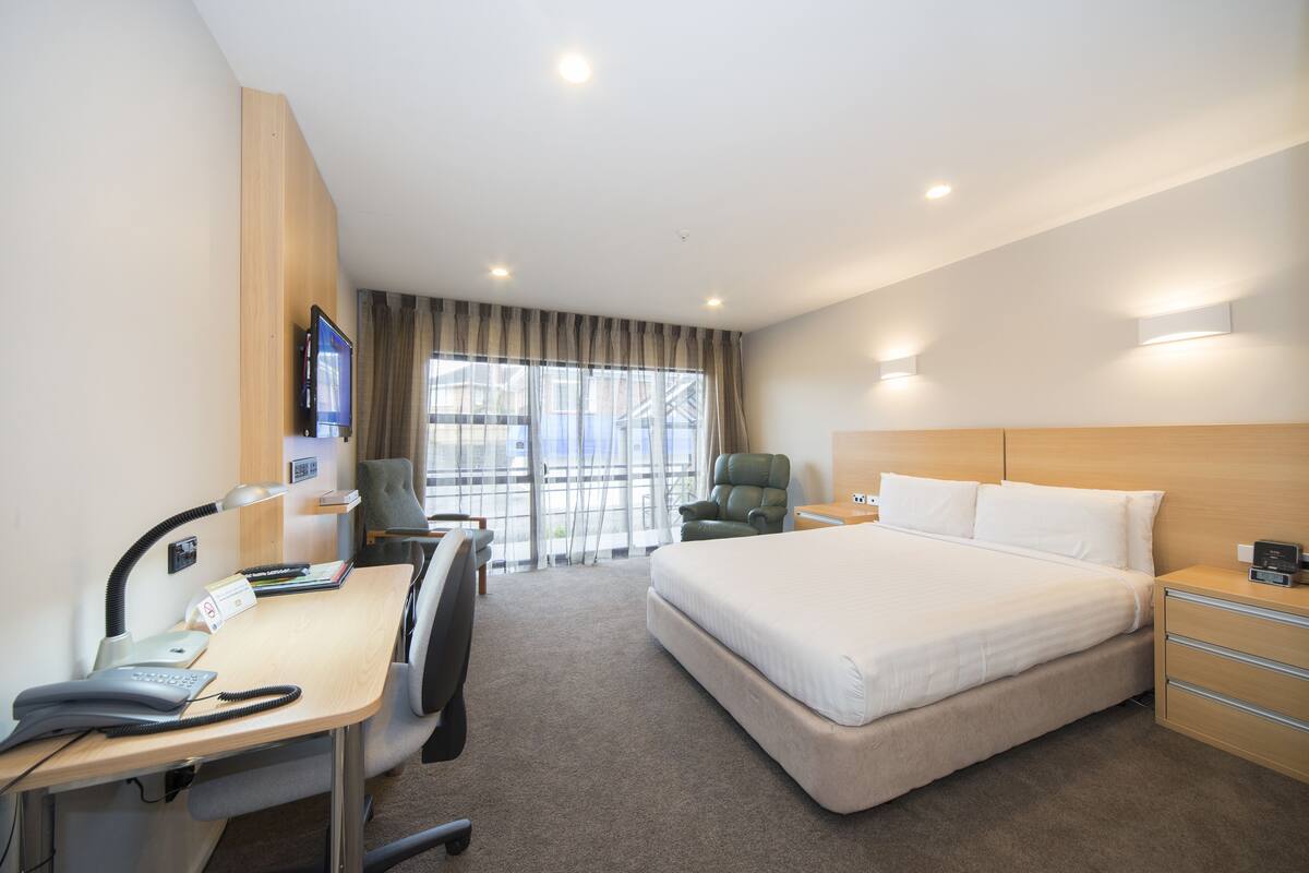 A hotel room with a large bed, a desk with a computer, a chair, and a TV.