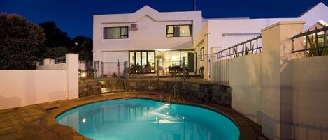 Una casa moderna con piscina, escalones de piedra y un patio bien iluminado.