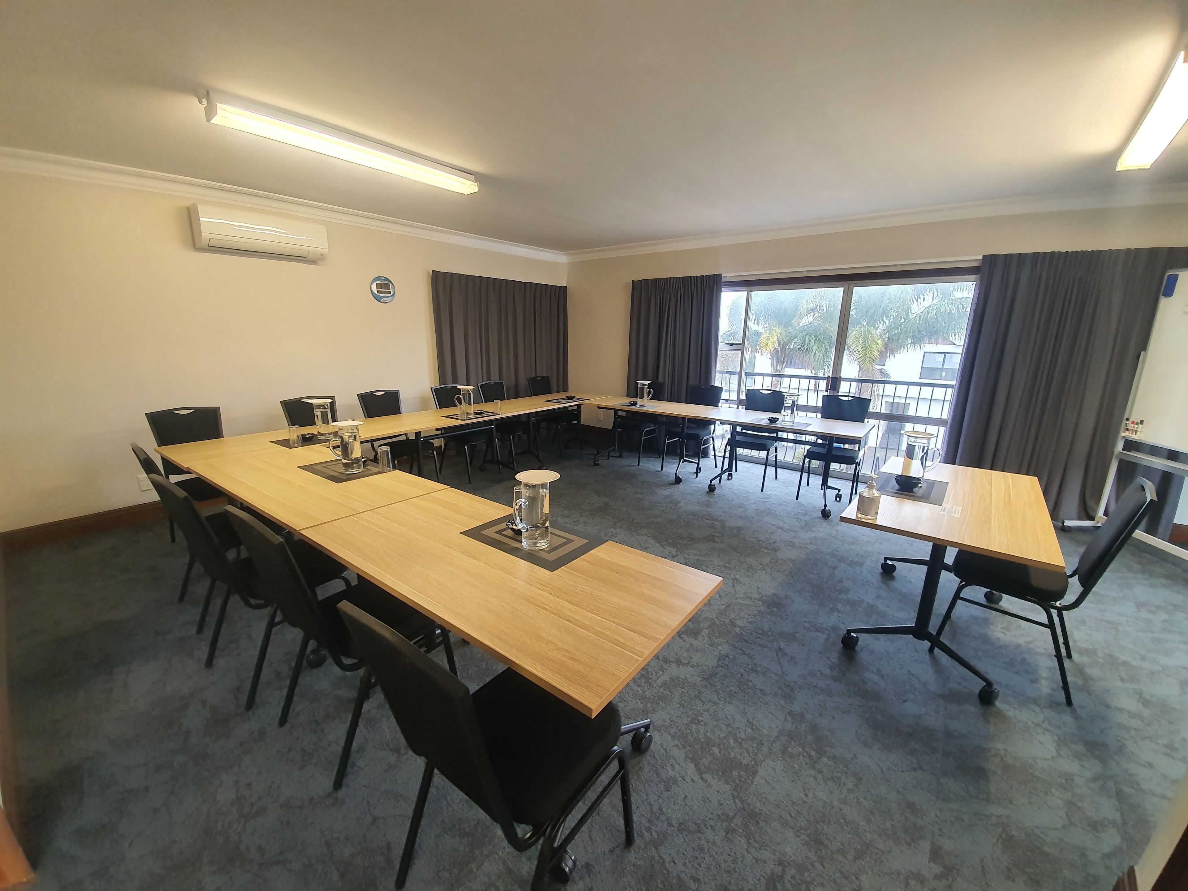 A conference room with a long table, multiple chairs, and a large window with curtains.