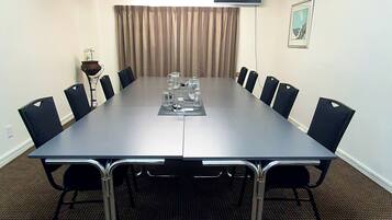 Un salón de conferencias con una larga mesa, sillas, un ventilador de techo y una ventana con cortinas.