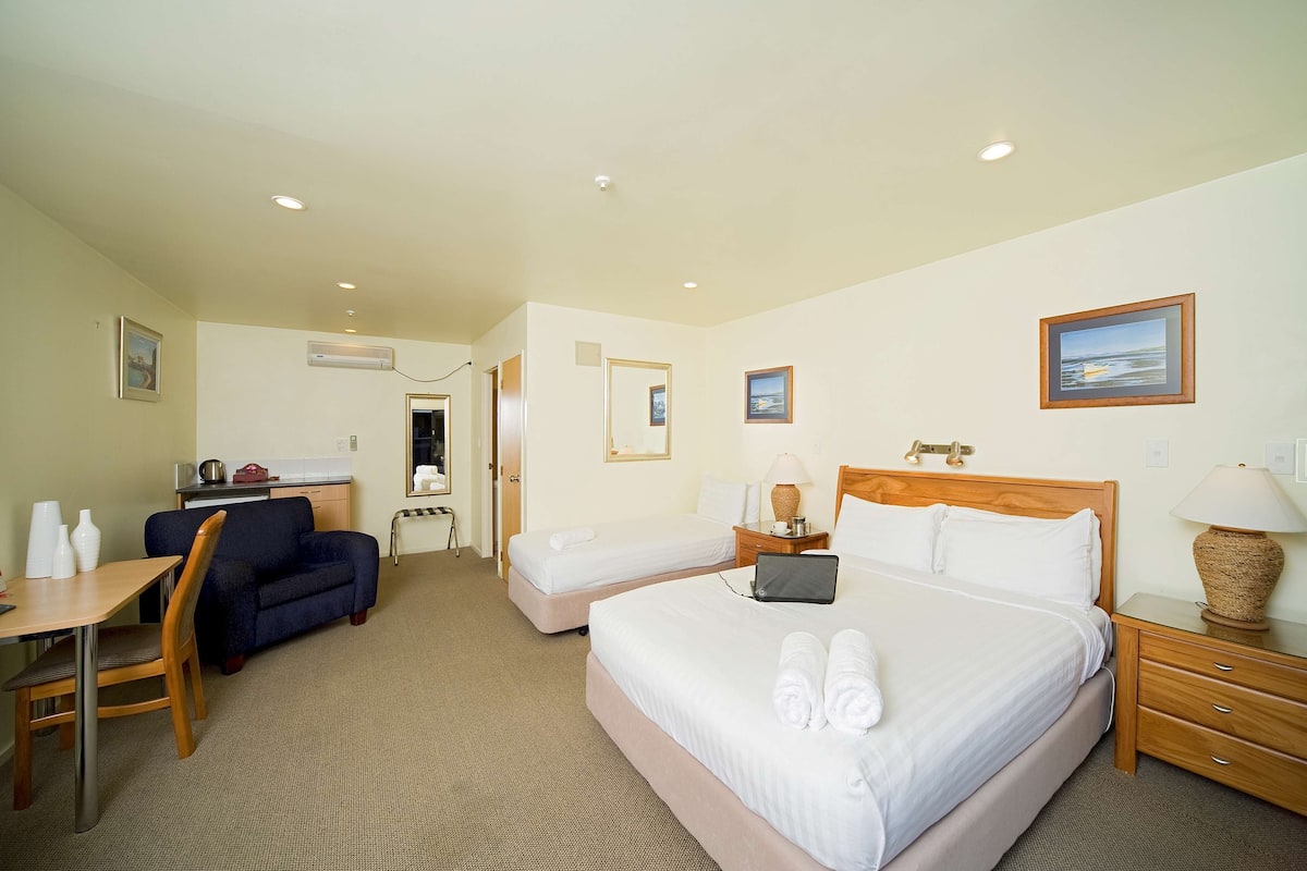 A hotel room with two beds, a desk, a chair, a small kitchenette, and a bathroom.