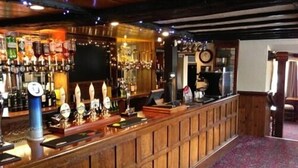 A bar area with wooden paneling, a counter with taps, and a variety of bottles and glasses. - The Charlton Inn (Blandford Forum)
