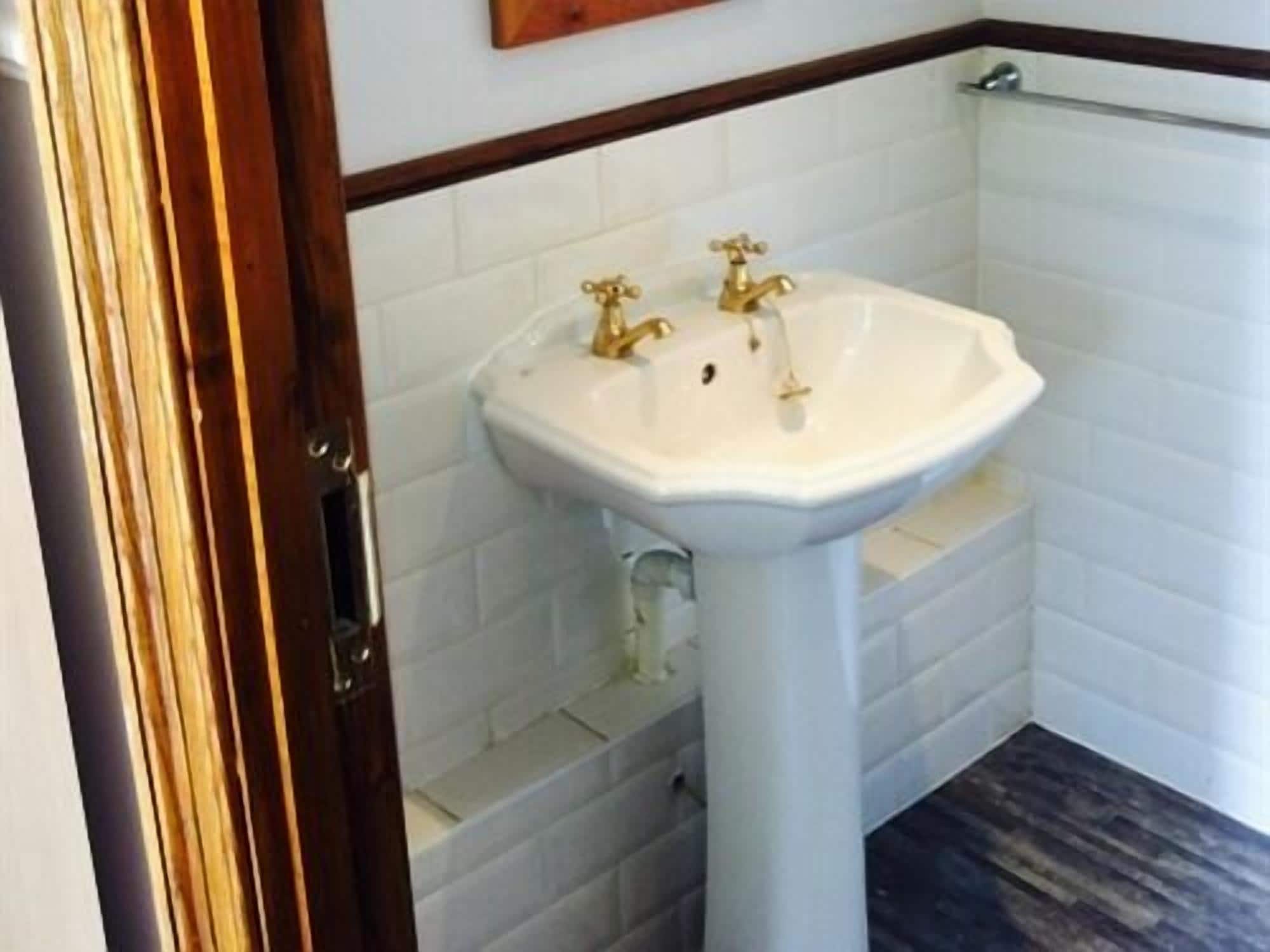 A bathroom with a white pedestal sink, a wooden door frame, and white tiled walls.