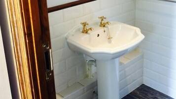 A bathroom with a white pedestal sink, a wooden door frame, and white tiled walls.