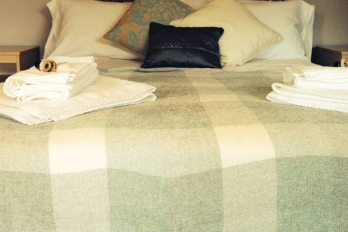 A neatly made bed with a checkered bedspread, pillows, and folded towels.