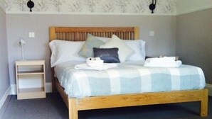 A bedroom with a wooden bed, a nightstand, and a wall-mounted lamp. - The Charlton Inn (Blandford Forum)