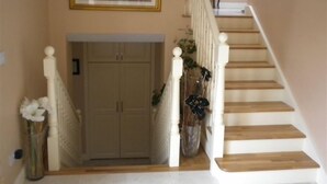 Una escalera con balaustres blancos y acabado de madera, que conduce a un rellano con un cuadro enmarcado sobre una puerta.