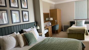 A hotel room with a bed, a desk, a chair, a wardrobe, and framed artwork on the wall.