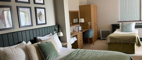 Une chambre d’hôtel comprenant un lit, un bureau, une chaise, une armoire et des œuvres d’art encadrées accrochées au mur.