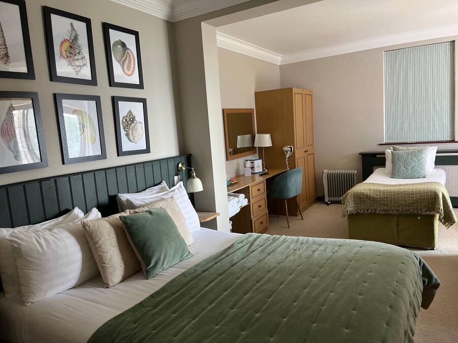 A hotel room with a bed, a desk, a chair, a wardrobe, and framed artwork on the wall.