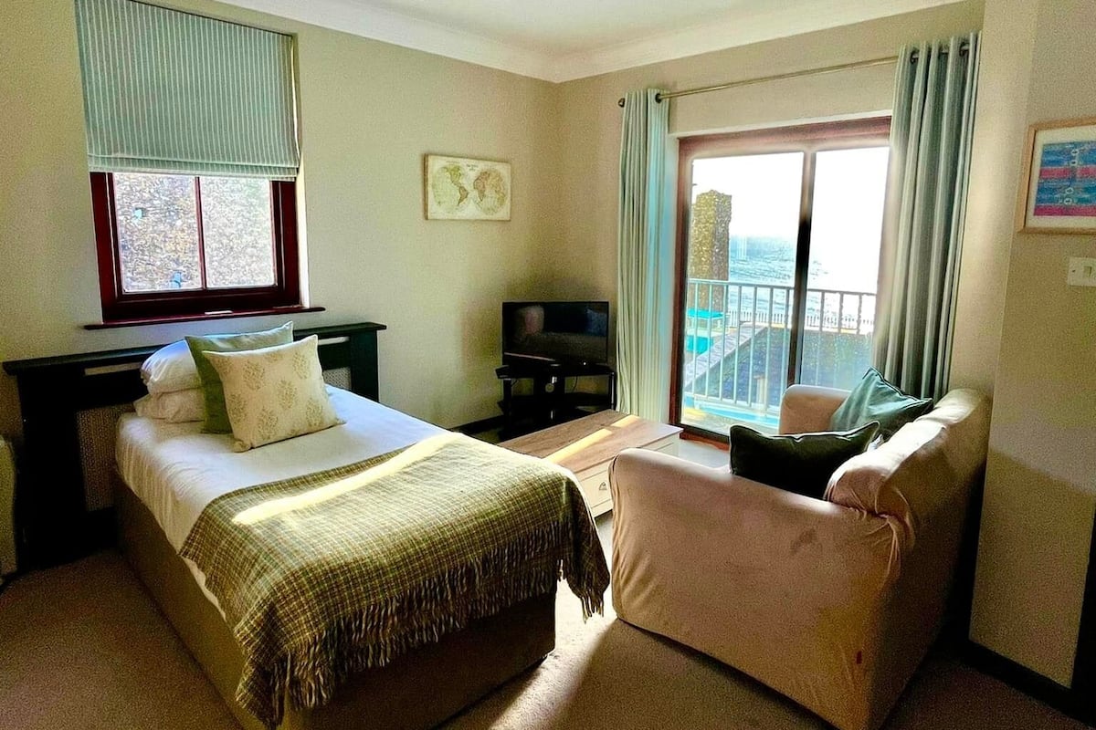 Habitación de hotel con cama, sofá, televisión y ventana con cortinas.