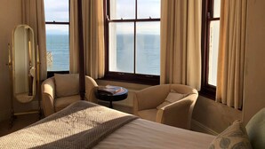 Habitación de hotel con cama, dos sillones, una mesa redonda y un ventanal con vistas al mar.