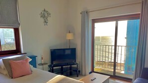 Habitación de hotel con cama, televisor, escritorio, silla y balcón con vistas.