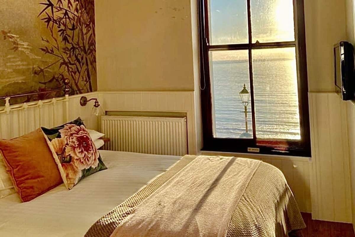 Un dormitorio con un ventanal grande, una cama con un cojín floral, una colcha tejida y una araña.