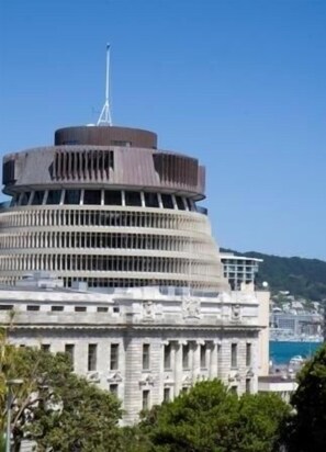 A large, circular building with a central tower and multiple balconies, surrounded by greenery and a body of water in the background. - Quest on Lambton (Wellington)