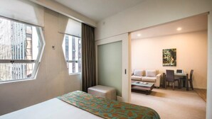 A hotel room with a large bed, a small sofa, a desk with a chair, and a window with curtains. - Quest on Lambton (Wellington)