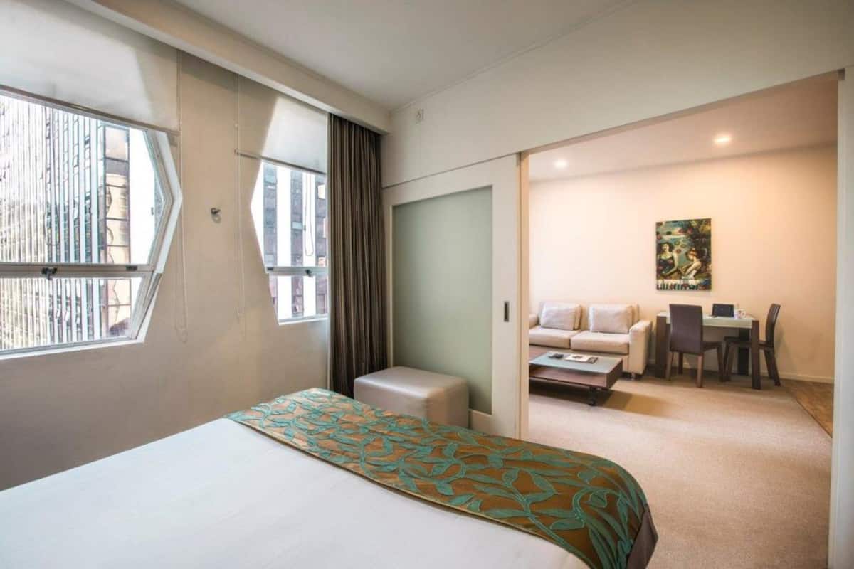 Une chambre d’hôtel avec un grand lit, un petit canapé, un bureau avec une chaise et une fenêtre avec des rideaux.