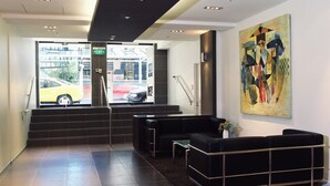 A modern lobby with a reception desk, black leather seating, a staircase, and a large abstract painting. - Quest on Lambton (Wellington)