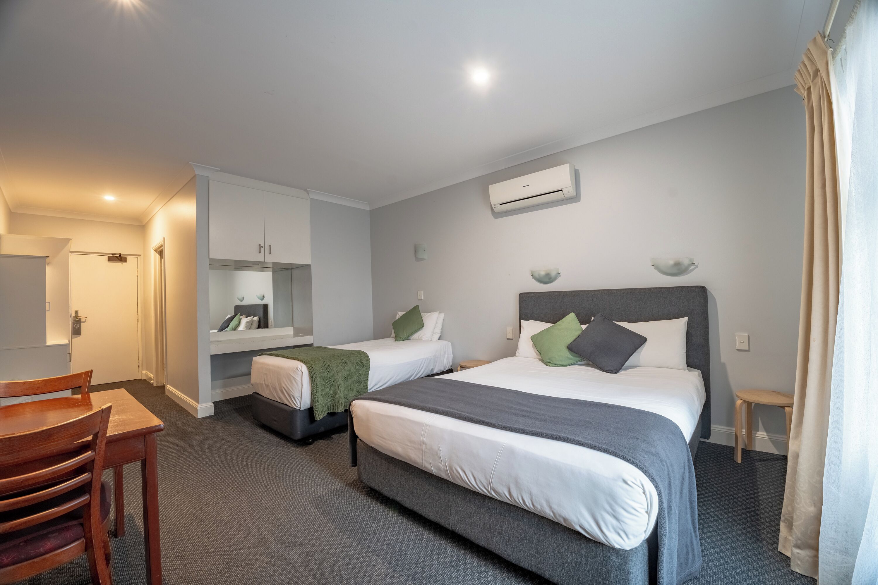 Une chambre d’hôtel avec deux lits, un bureau, une chaise, un miroir et un appareil de climatisation.