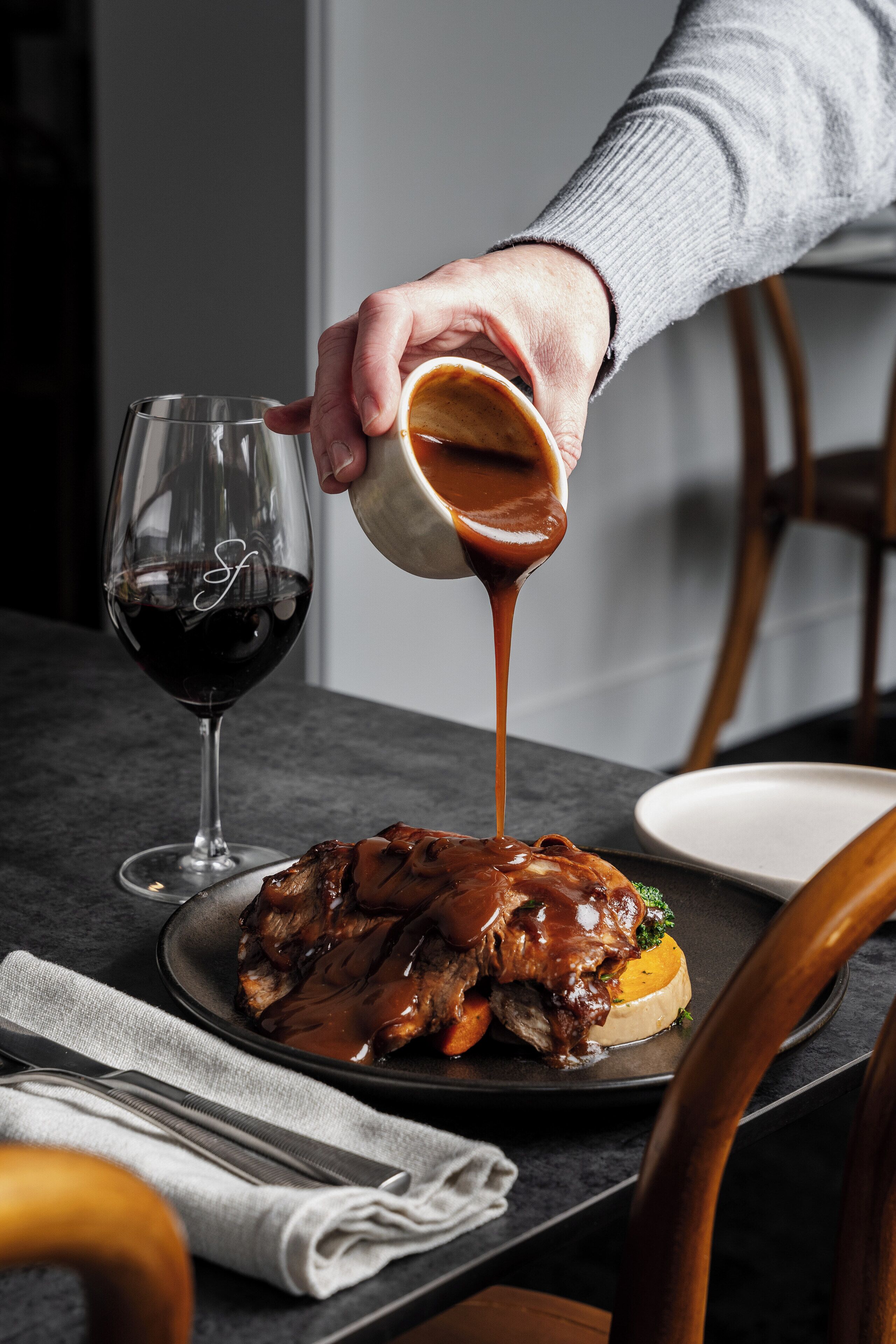A person pouring sauce over a dish on a plate.