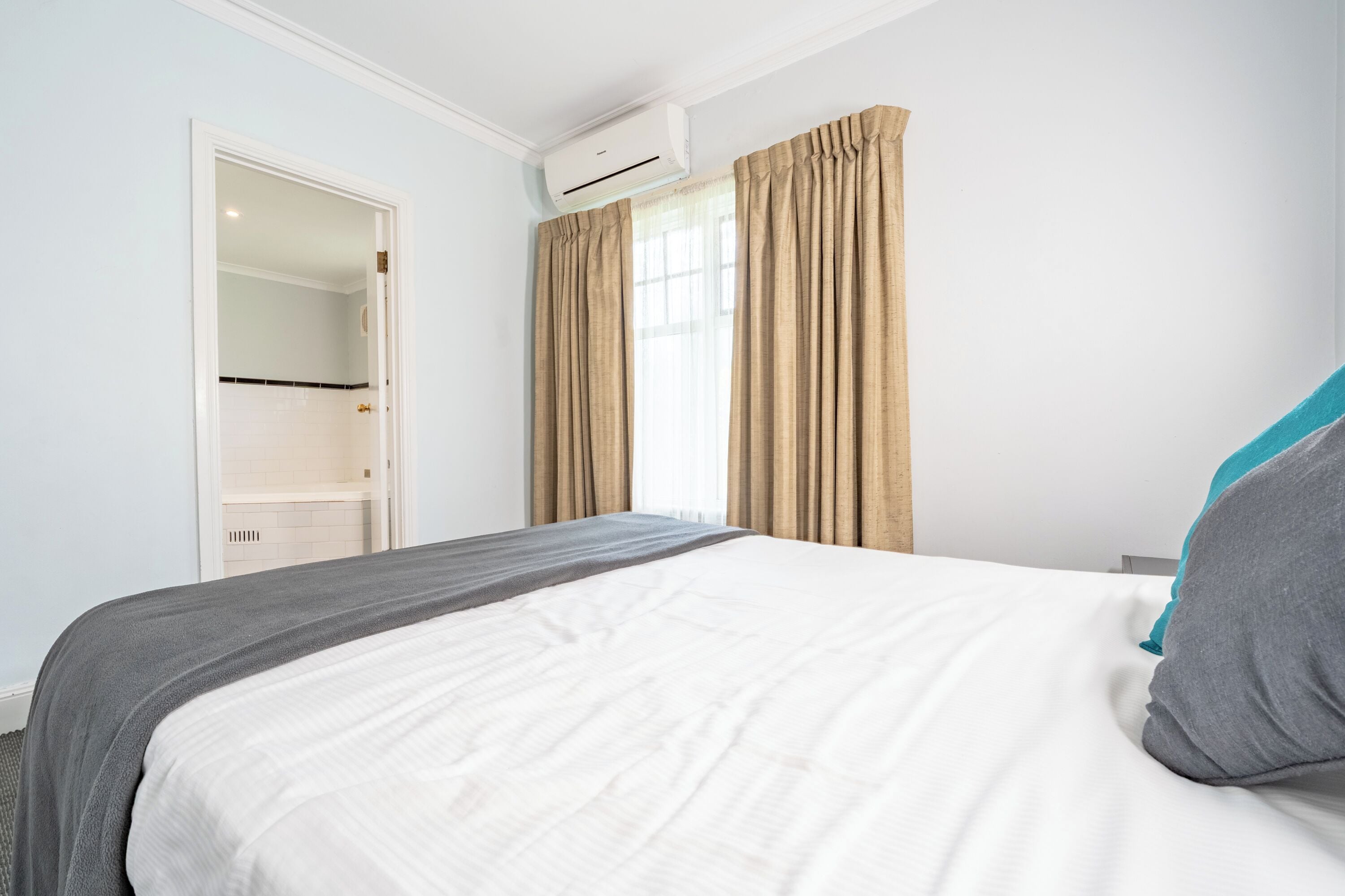A bedroom with a bed, a wardrobe, an air conditioning unit, and a window with curtains.