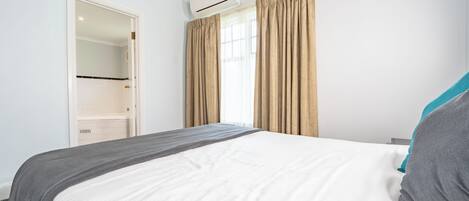 A bedroom with a bed, a wardrobe, an air conditioning unit, and a window with curtains.