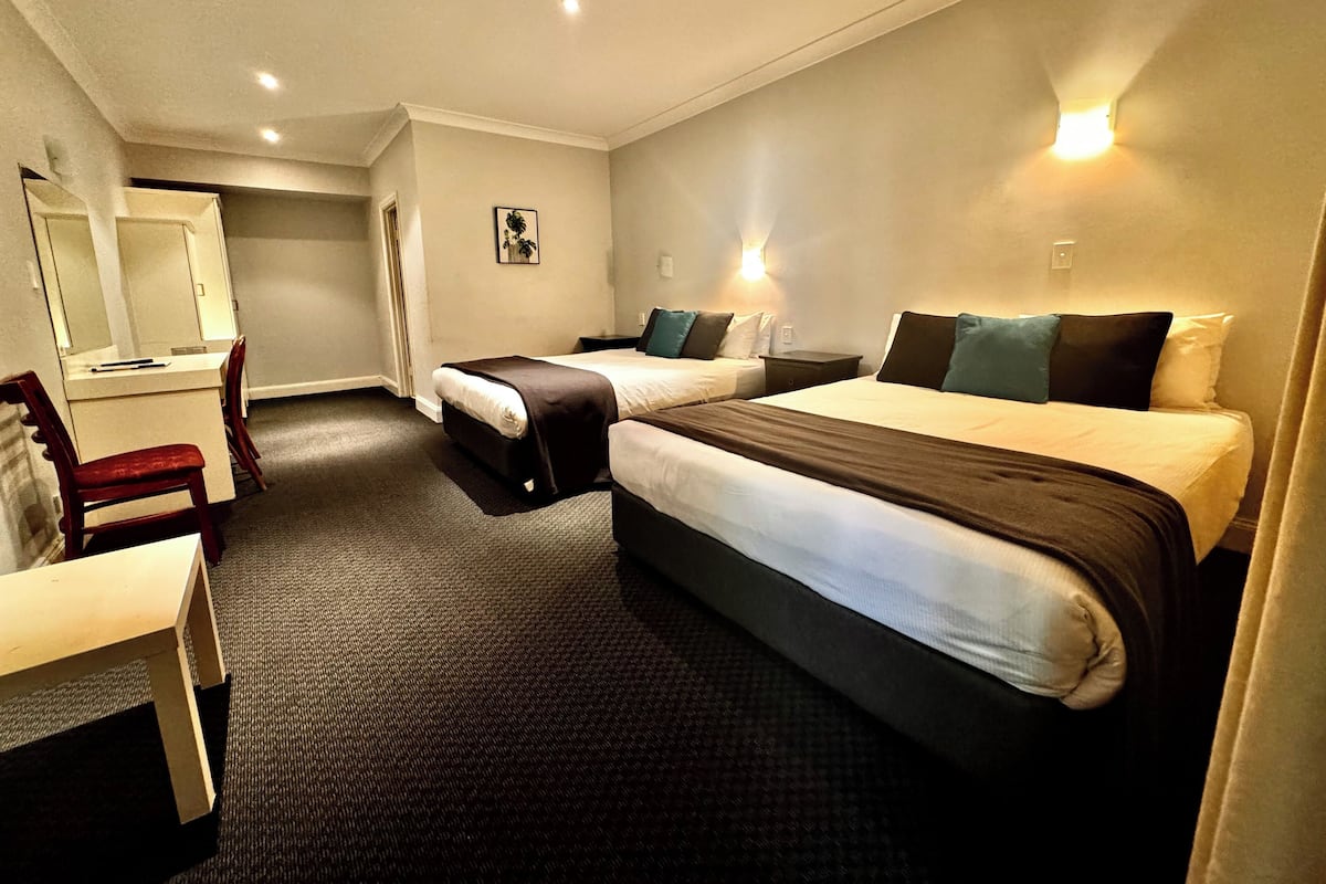 A hotel room with two beds, a desk, a chair, and a mirror.