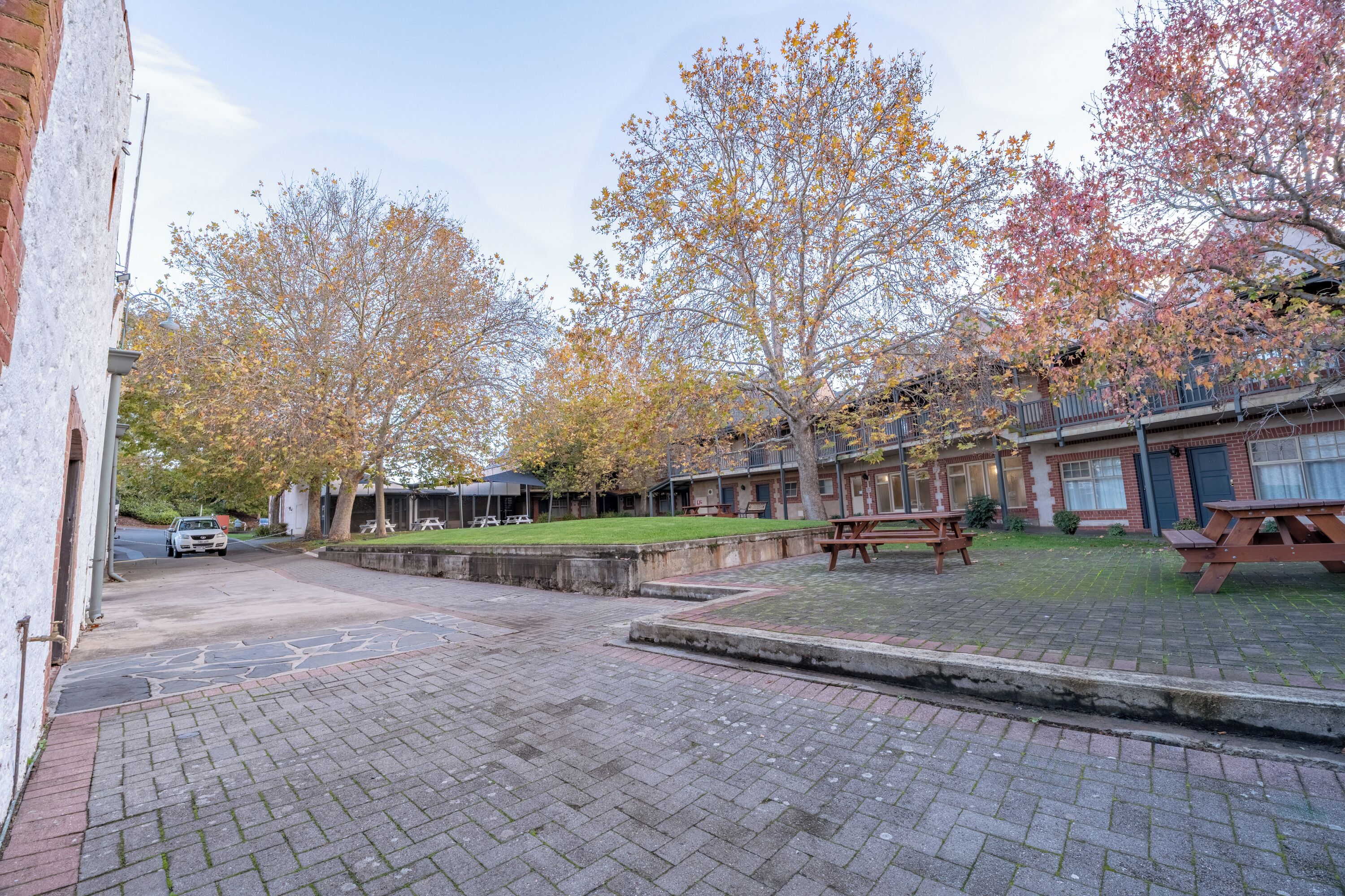 A courtyard with brick paving, picnic tables, and trees with autumn foliage.
