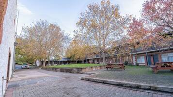 A courtyard with brick paving, picnic tables, and trees with autumn foliage.