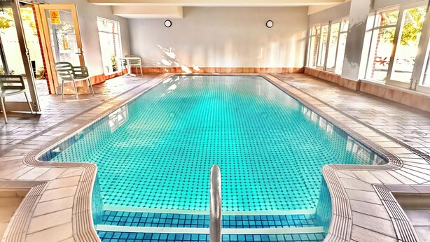 Une piscine intérieure à l’eau claire, dotée d’un sol carrelé et d’une rambarde de sécurité en métal.
