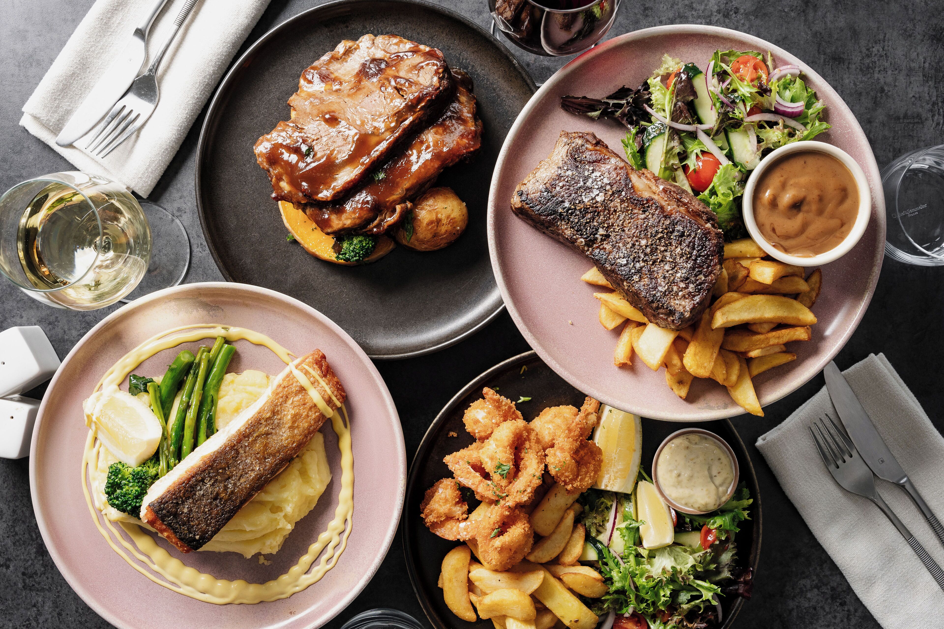 Une table où l’on trouve divers plats, notamment du poisson, des frites et une salade.