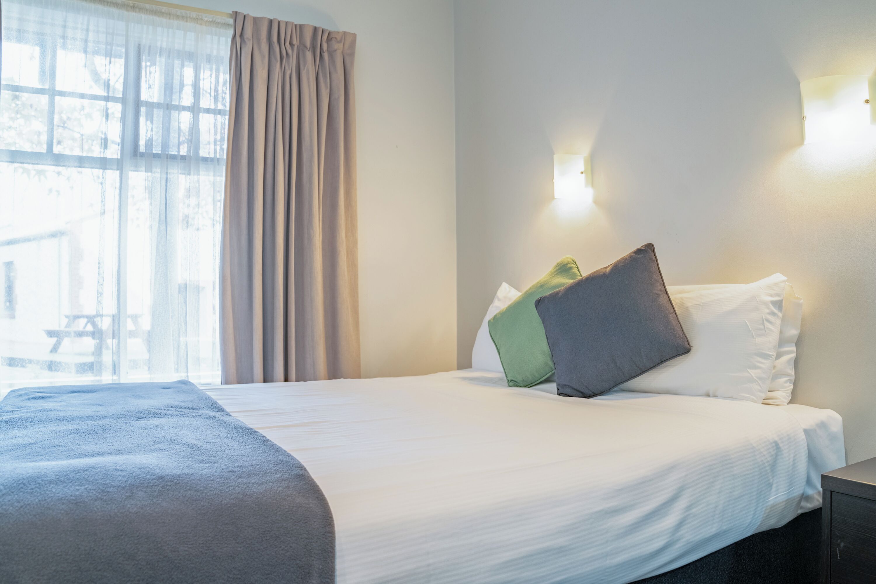 Una cama bien hecha con edredón blanco, una manta gris y dos almohadas en tonos verde y gris.