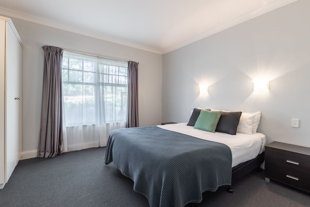 A bedroom with a large bed, a nightstand, and a window with curtains.