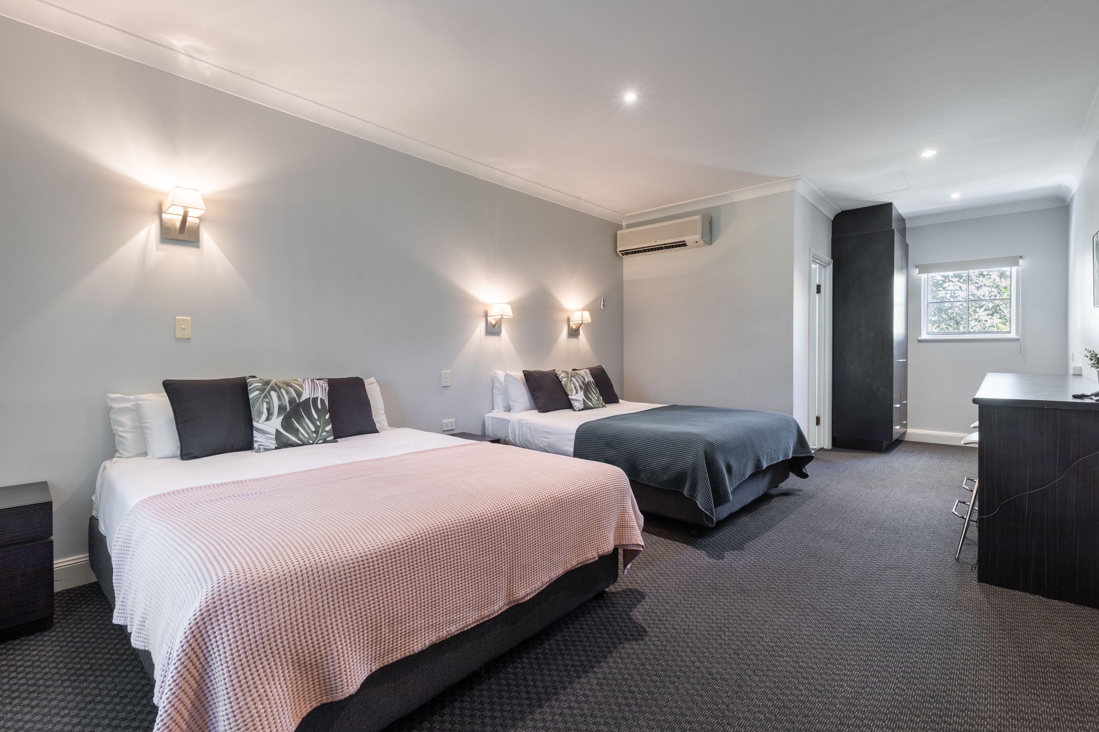 A hotel room with two beds, a desk, and a window.