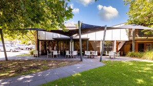 Un espace extérieur aménagé avec des tables et des chaises, une terrasse couverte et un bâtiment à la façade en briques, doté d’un escalier.